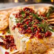 some crackers and cheese are on a plate with red sauce, garnished with herbs