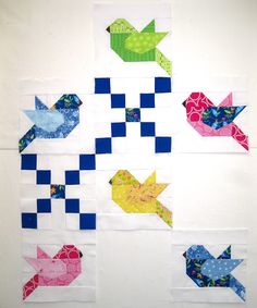 four different colored birds on a white wall with blue and pink squares in the background