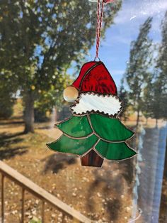 a stained glass christmas ornament hanging from a window with trees in the background