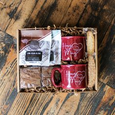 two red coffee mugs in a gift box on a wooden table with writing and stickers