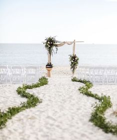 an outdoor ceremony set up on the beach with chairs and greenery in front of it