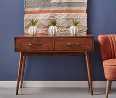 an orange chair sits next to a wooden table with two plants on it and a blue wall behind it