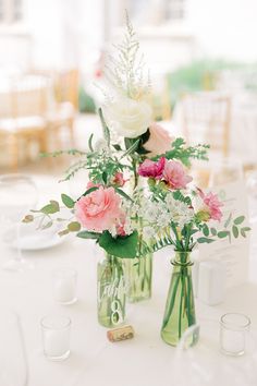 two vases filled with pink and white flowers on top of a table next to glasses