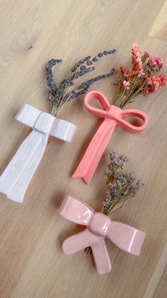 three pink and white bows are sitting on a table next to dried flowers, with one tied up in the shape of a cross