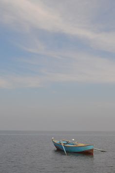 a blue boat floating on top of a large body of water under a cloudy sky