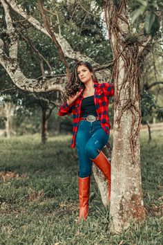 a woman leaning against a tree wearing boots