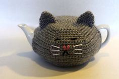 a crocheted cat tea cosy with a white cup in the shape of a teapot