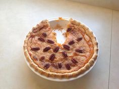 a pie sitting on top of a white plate covered in pecans and other toppings