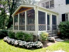 a screened porch in front of a house with white flowers and bushes around it on the lawn