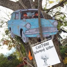 an old blue car hanging from the side of a tree in front of a sign that says caution whimping willows