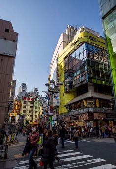 many people are crossing the street in front of some tall buildings with glass on them