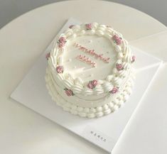 a white cake with pink flowers on it sitting on top of a card that says happy birthday