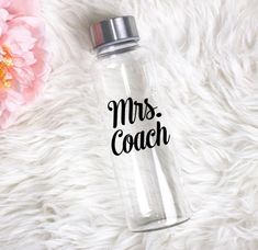 a clear water bottle with the words mrs coach on it next to a pink flower