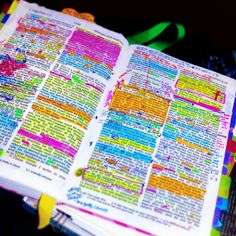 an open bible with colorful pages and writing on the page is sitting on a table