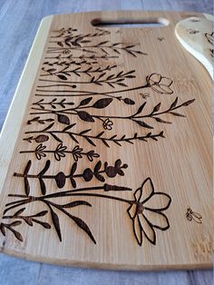 a wooden cutting board with flowers and leaves etched on the surface next to a spoon