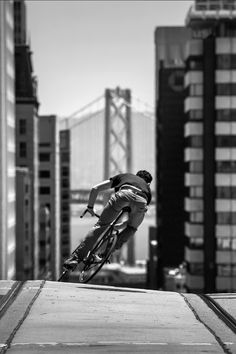 a man riding a bike up the side of a ramp in front of tall buildings