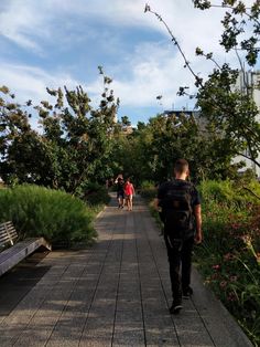 two people walking down a path next to trees and plants on either side of the walkway