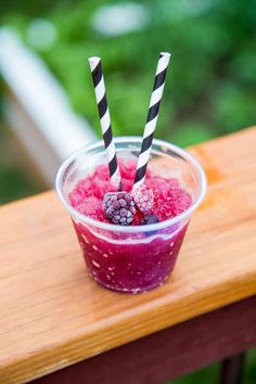 two straws sticking out of the top of a smoothie with raspberries and blueberries