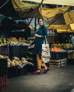 a woman is walking through an outdoor market carrying a bag and shopping for fruit in baskets