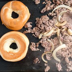 two hamburgers and onion rings are being cooked on a black grill pan with oil