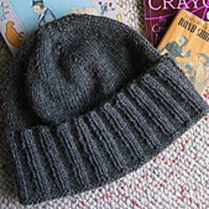 a gray knitted hat sitting on top of a white blanket next to a book