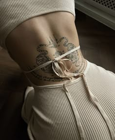 the back of a woman with tattoos on her upper body and lower back, wearing a beige ribbed top