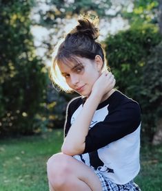 a young woman sitting on the ground with her hand under her chin and looking at the camera