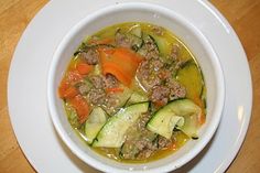 a white bowl filled with meat and veggies on top of a wooden table