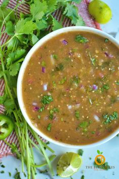 a close up of a bowl of soup with cilantro and limes on the side