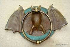 a bronze bat with wings on a blue and gold plated wall mounted hook in the shape of a circle