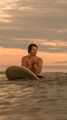 a man sitting on a surfboard in the ocean with his hands clasped to his chest