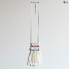 a white necklace with fringes hanging from it's side on a chain against a wall