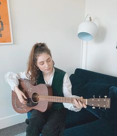 a woman sitting on a couch playing an acoustic guitar