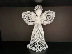 a white crocheted angel statue sitting on top of a black table next to a wall