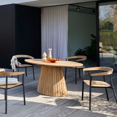 a wooden table with four chairs around it on a wood deck next to a building