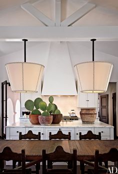 a dining room table and chairs in front of a kitchen island with lights hanging from the ceiling