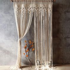 a macrame wall hanging next to a plant with orange flowers in the foreground