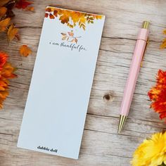 a notepad sitting on top of a wooden table next to flowers and a pen