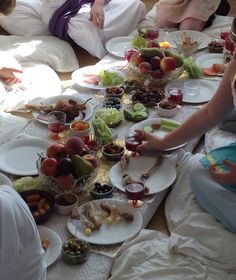 several people sitting at a table with plates and bowls of food on it, while others sit down to eat