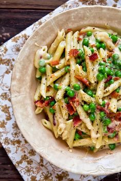 a bowl filled with pasta and peas on top of a wooden table next to a napkin