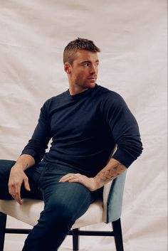 a man sitting on top of a chair with his hands in his pockets and looking off to the side