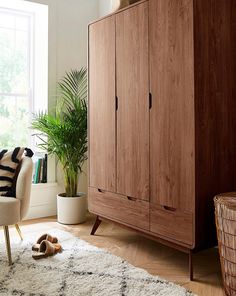 a wooden cabinet sitting in the corner of a room next to a chair and potted plant