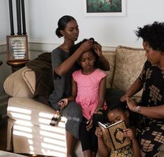 three women sitting on a couch while one woman combs another's hair