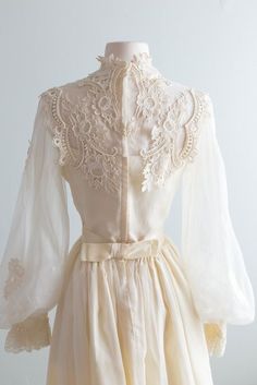 a white dress with sheer sleeves and lace on the neckline is shown in front of a mannequin