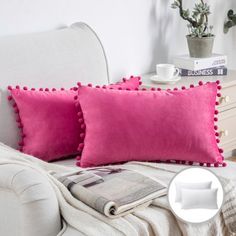 two red pillows sitting on top of a white couch next to a magazine and potted plant