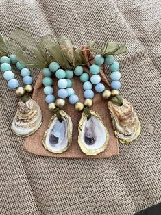 three seashells with blue beads and green leaves on a burlap surface