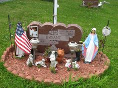 a statue of the virgin mary and baby jesus in front of a headstone with flags