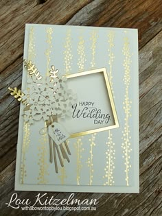 a card with gold foil on it and some flowers in the middle, sitting on a wooden table