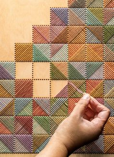 a person's hand is pointing at a patchwork pattern on a wall that appears to be made out of wood