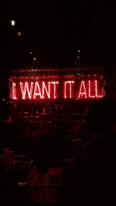 a neon sign that says i want it all in the dark with people sitting around